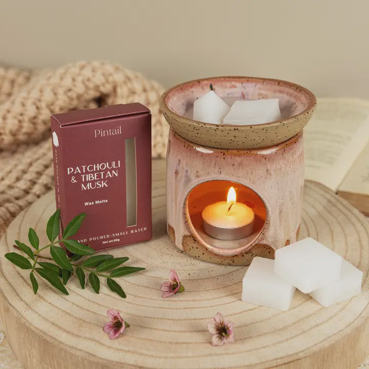 Wax melt burner with a lit candle, surrounded by wax melts and a box labeled &