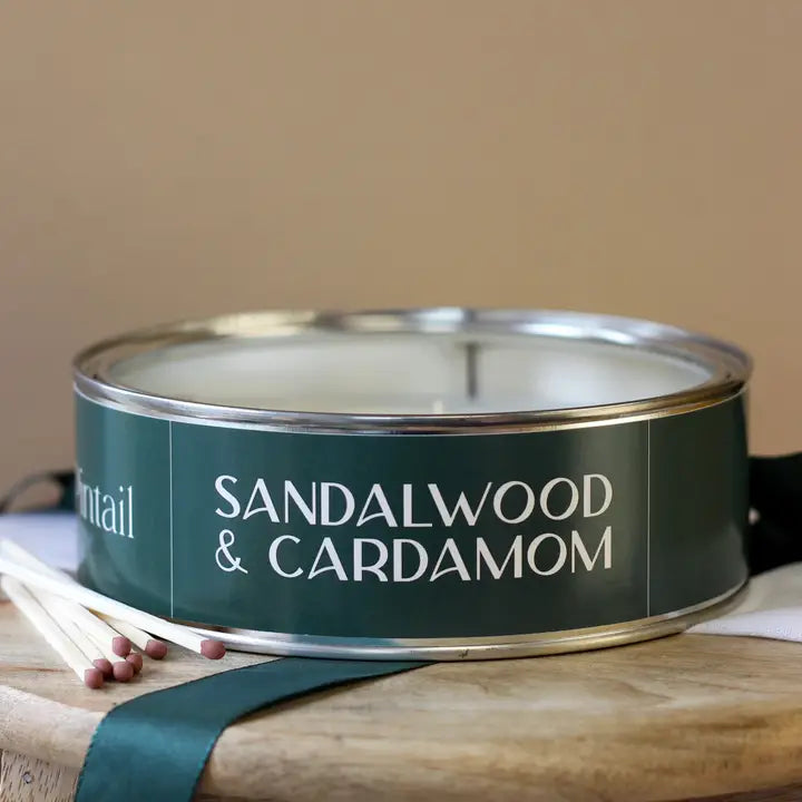 Sandalwood &amp; Cardamom candle in a green tin with matches on a wooden surface