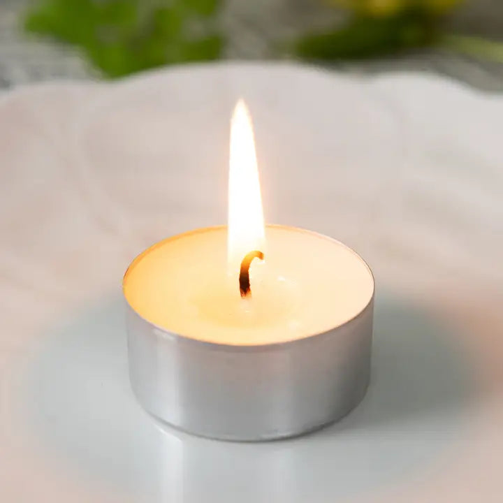 Tea light candle on a white surface with a blurred green background
