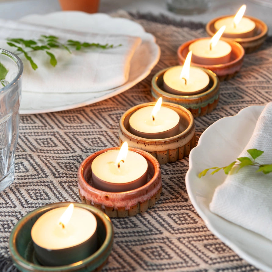 Candle holders with lit candles on a patterned tablecloth with plates and glasses.
