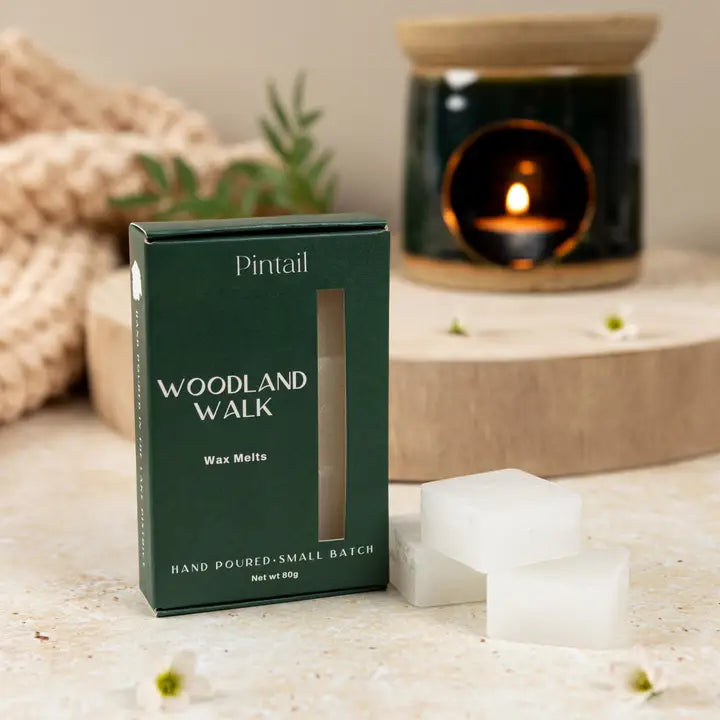 Pintail Woodland Walk wax melts packaging with wax melts on a surface, blurred candle in the background.