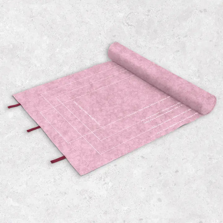 A pink textured fabric puzzle mat with white printed grid lines and small red ties, shown partially unrolled on a light gray textured background.