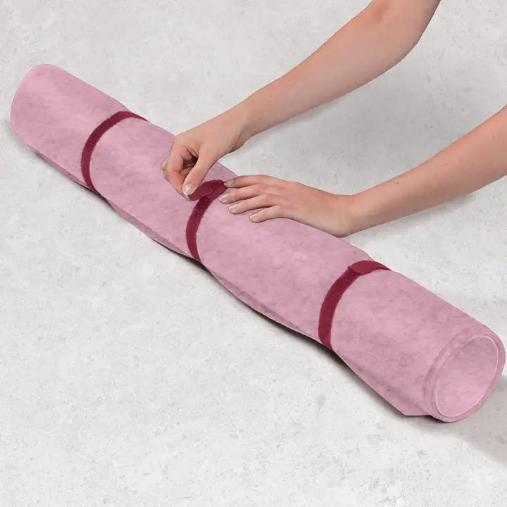 A pink rolled jigsaw puzzle mat with dark red elastic bands, held by a person&