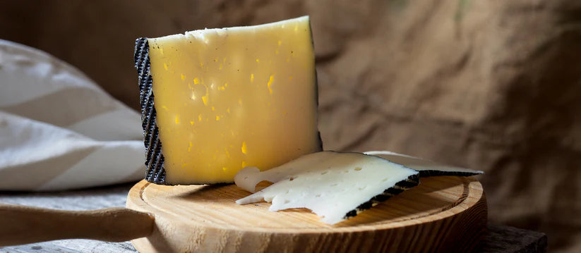 Block of cheese on a wooden board with a knife, against a blurred background