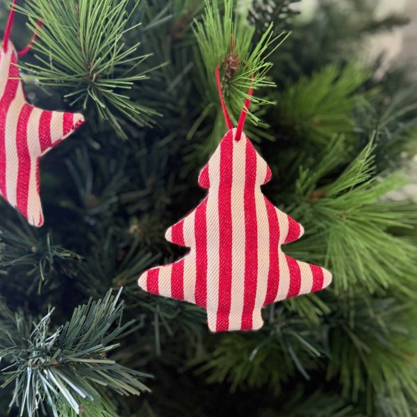 A red and cream striped fabric Christmas tree ornament hanging on a green pine tree branch.