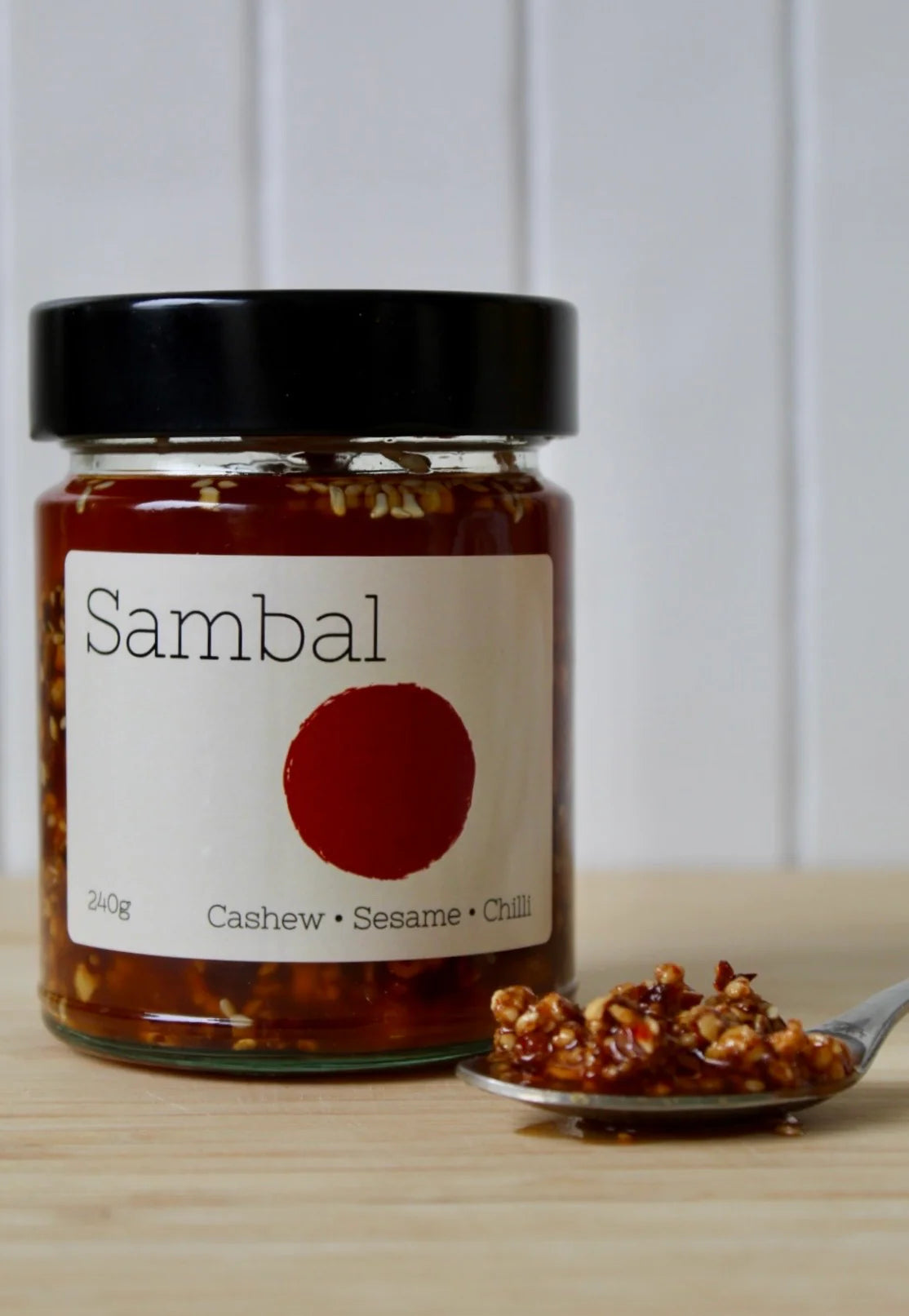 Jar of sambal with a spoonful of sambal on a wooden surface