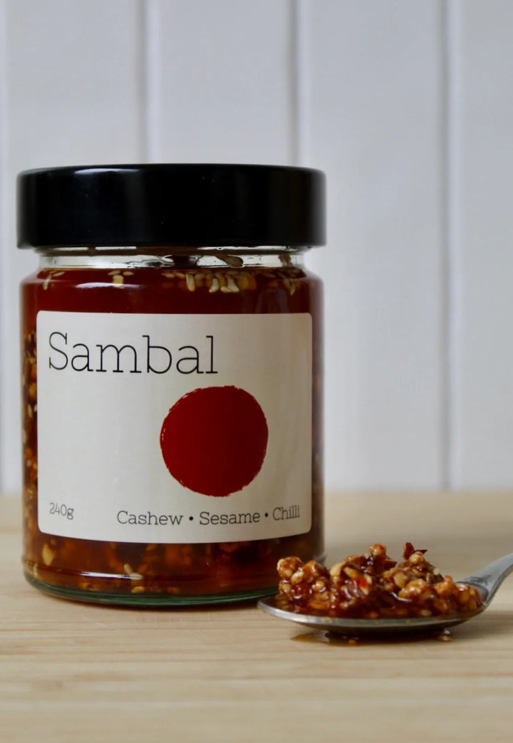 Jar of sambal with a spoonful of sambal on a wooden surface