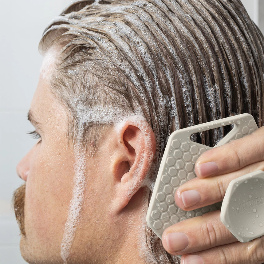 Person applying shampoo to their hair with a scrubber against a neutral background
