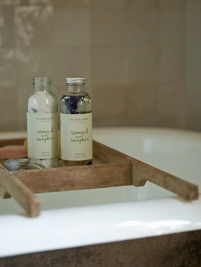 Two bottles of Plum &amp; Ashby seaweed and samphire bath salts on a textured surface with a wood board.