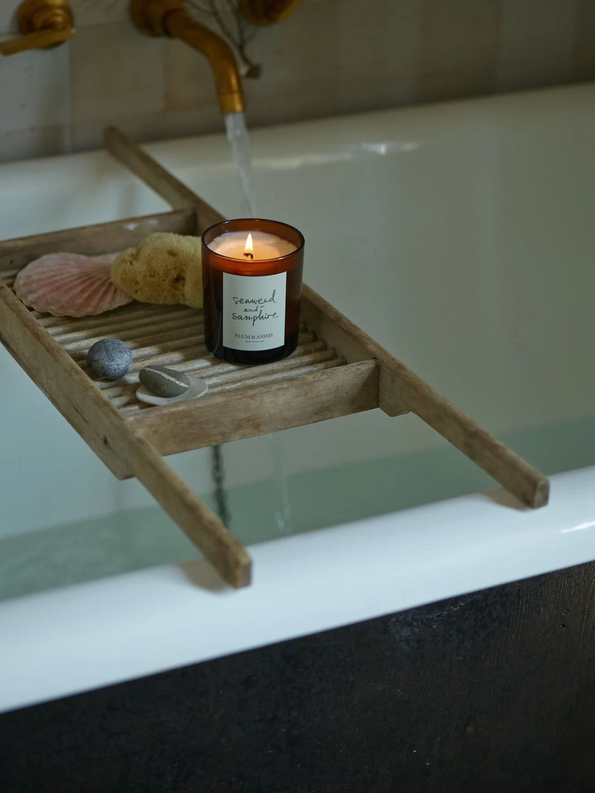 Seaweed and Samphire candle on a timber rack over a bathtub with shells and stones