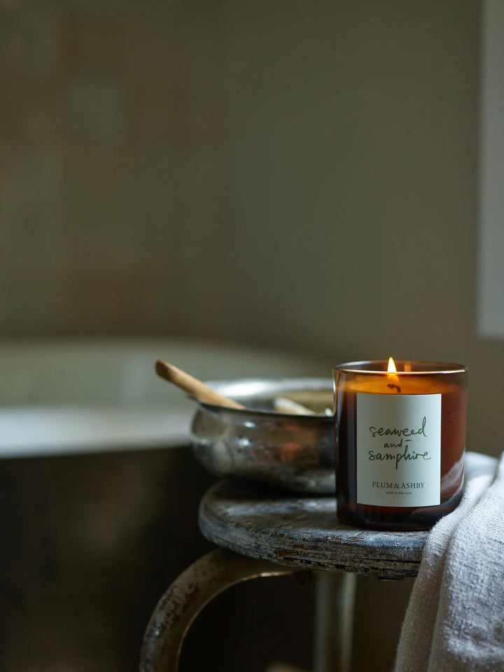 Lit seaweed and samphire candle on a timber stool with a steel bowl and white linen cloth