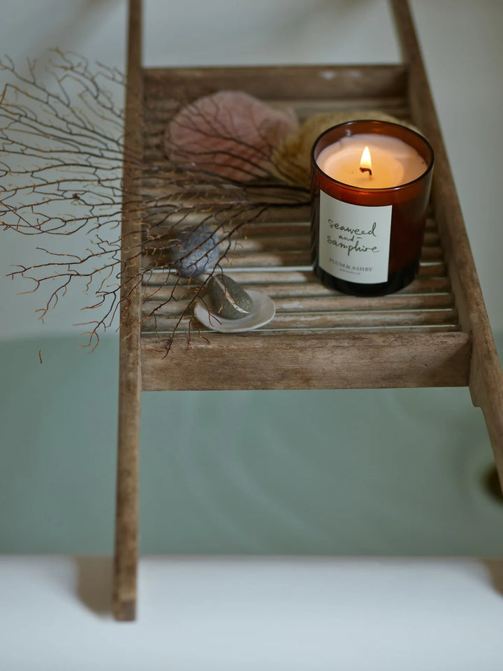 Lit seaweed and samphire candle on a timber rack over a bathtub with coral and stones