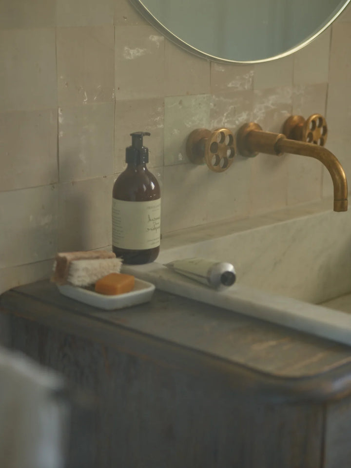Amber bottle of body lotion and a tube of hand cream on a bathroom basin
