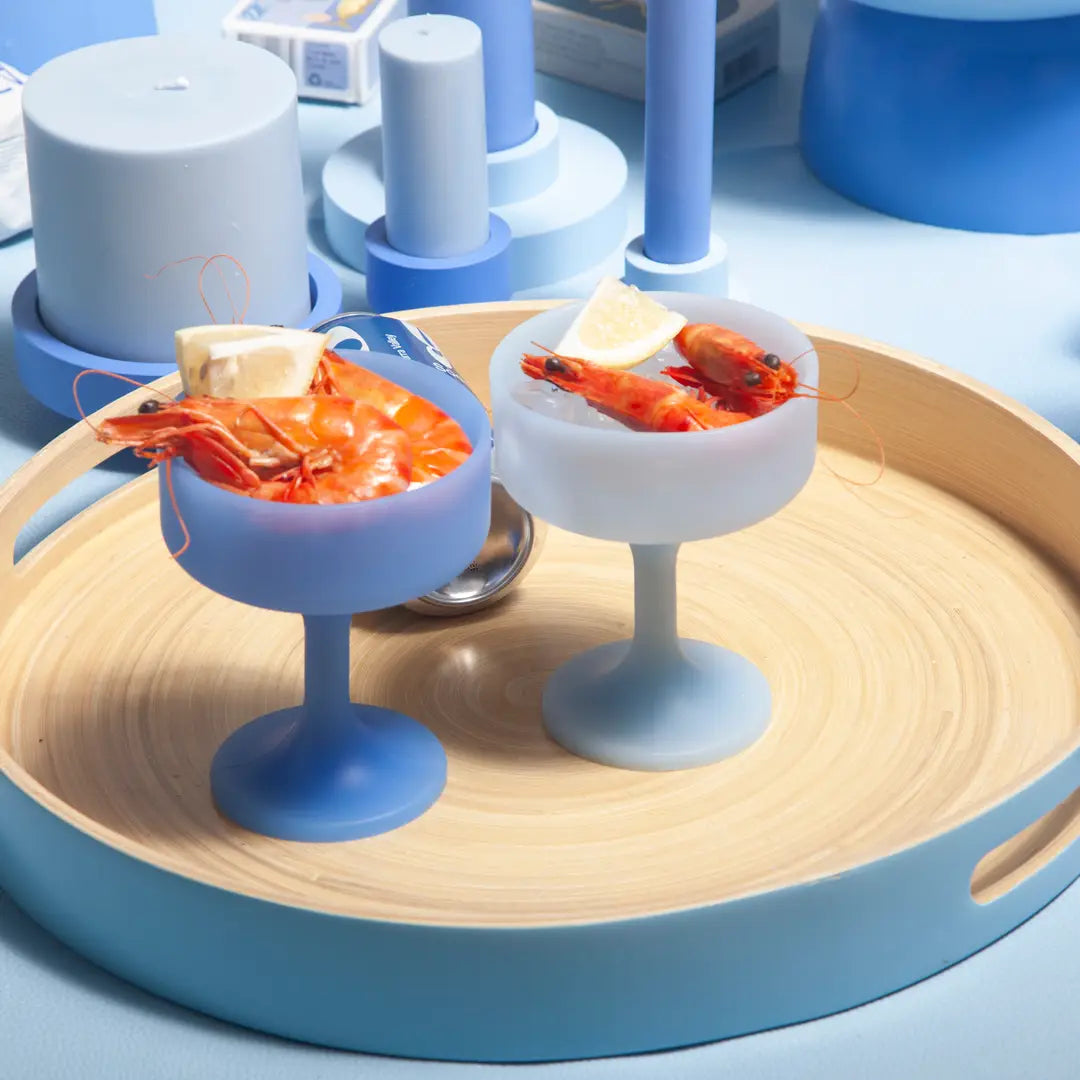 Two small silicone cocktail glasses with shrimp on a wooden tray