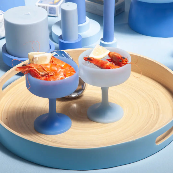 Two small silicone cocktail glasses with shrimp on a wooden tray