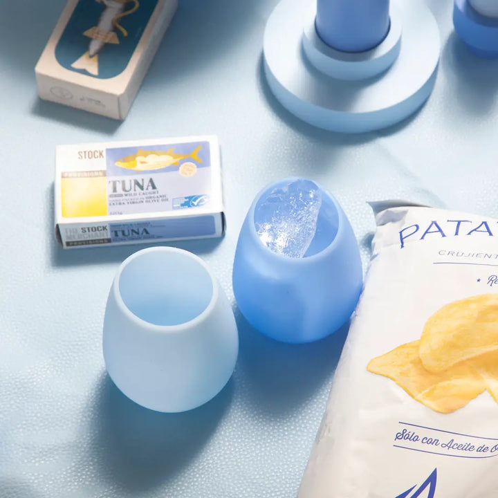 Blue and white silicone glasses on a light blue surface with a box of tuna and a packet of chips.