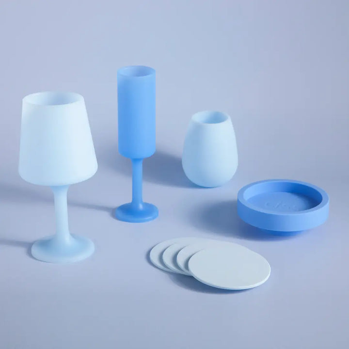 Set of blue silicone tableware including cups, a bowl, and coasters on a light gray background.