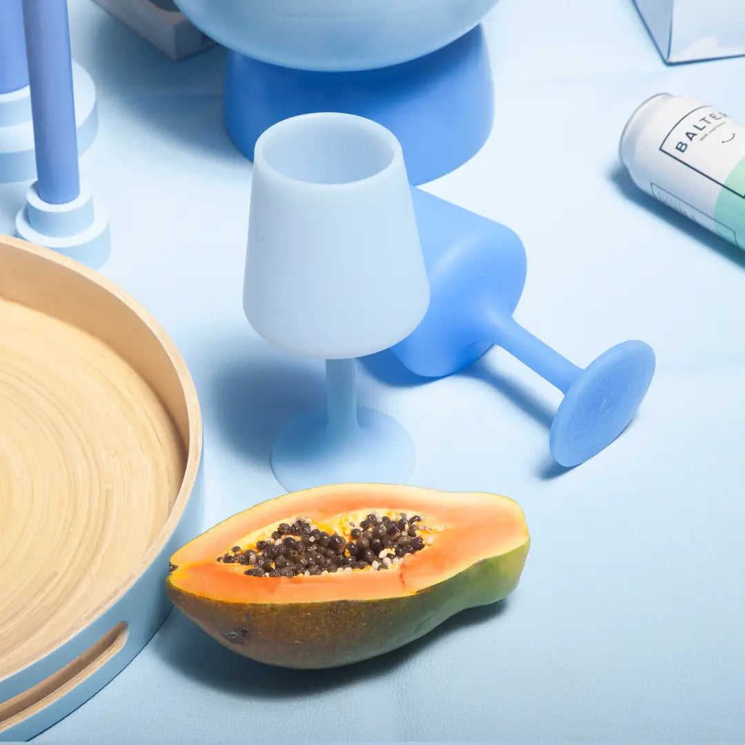 Papaya cut in half on a blue surface with a light blue and a mid-blue silicone wine glass in the background.