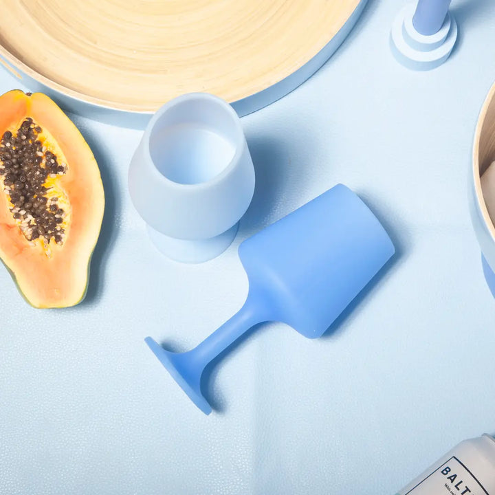 Blue silicone wine glass on a light blue surface with a halved papaya and a wooden bowl.