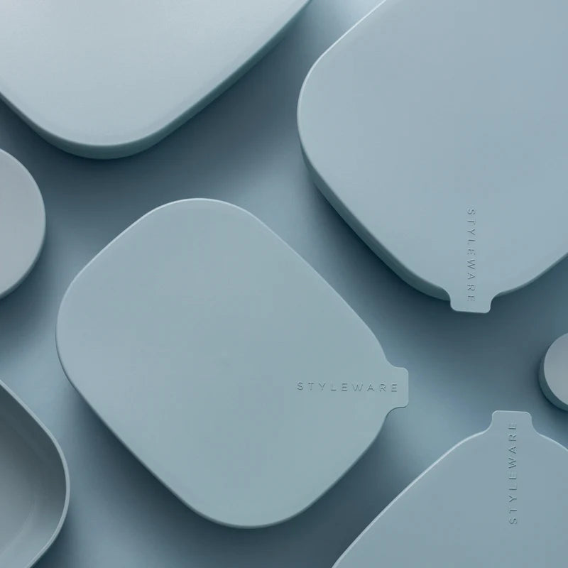 A close-up, top-down view of several light blue silicone or plastic accessory pieces with rounded organic shapes and small tab-like ends, arranged on a matching blue surface. The word STYLEWARE is printed vertically on one piece and appears on multiple pieces, indicating the visible brand.
