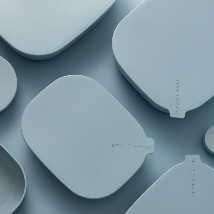 A close-up, top-down view of several light blue silicone or plastic accessory pieces with rounded organic shapes and small tab-like ends, arranged on a matching blue surface. The word STYLEWARE is printed vertically on one piece and appears on multiple pieces, indicating the visible brand.