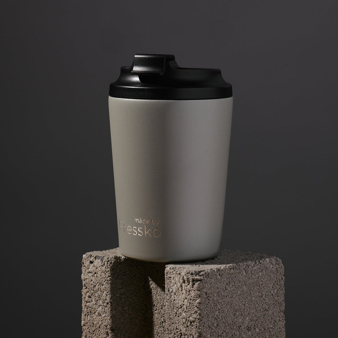 Gray tumbler with black lid on a concrete block against a dark background