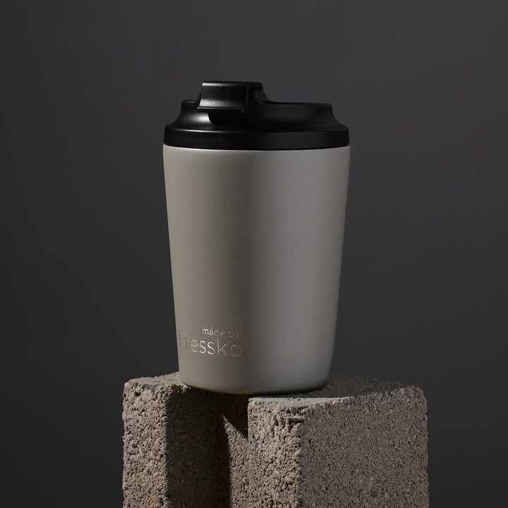 Gray tumbler with black lid on a concrete block against a dark background