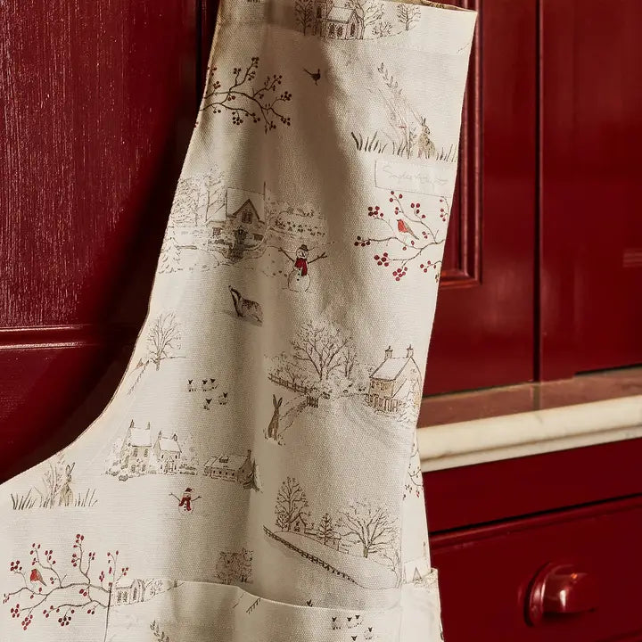 Fabric apron with snowy Christmas print hanging in front of a red cabinet