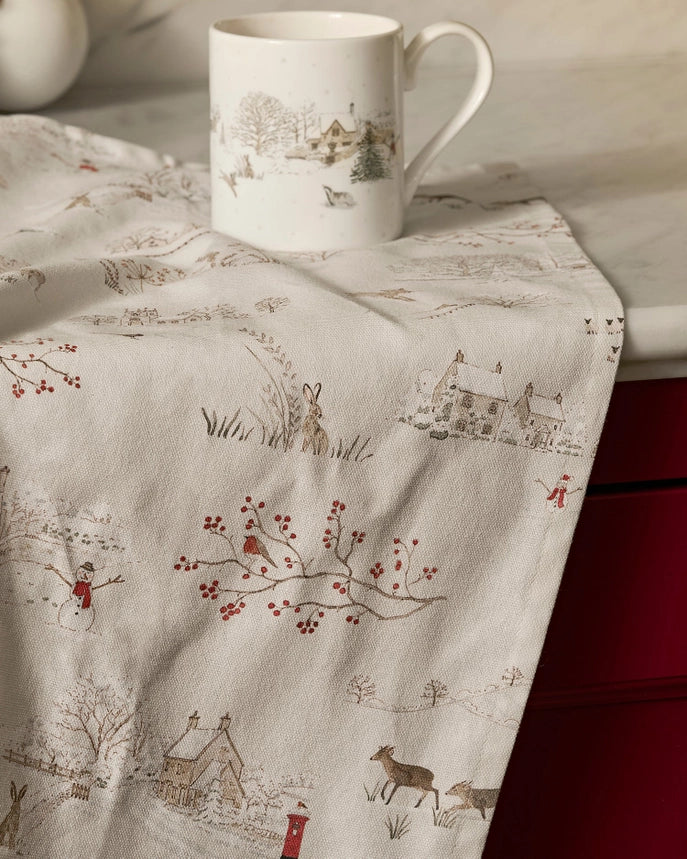 Cream coloured tea towel draped on a kitchen benchtop with winter Christmas themed print