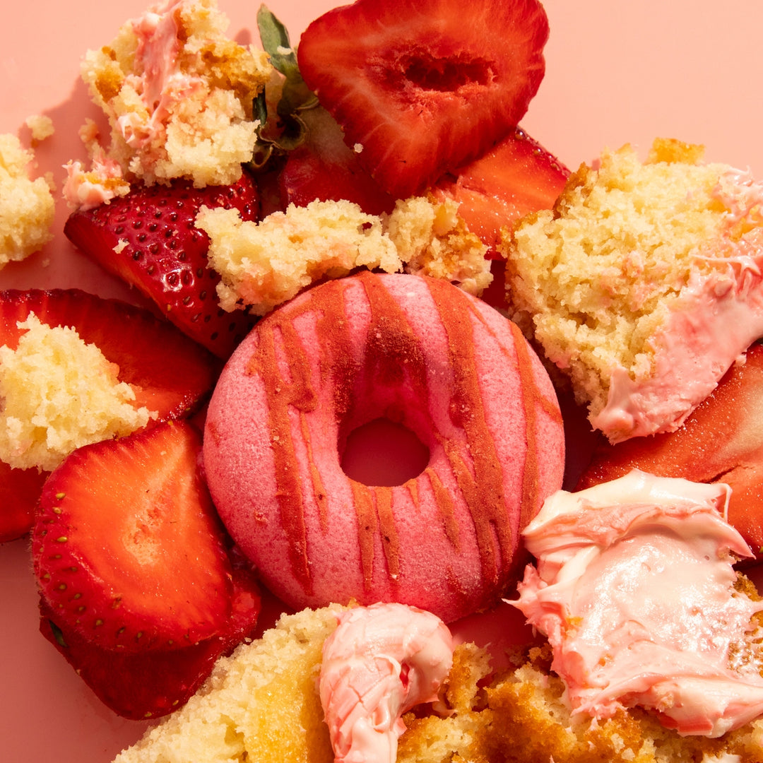 Delightful dessert arrangement with pink donut-shaped bath bomb, strawberries, and cake pieces on a pink background