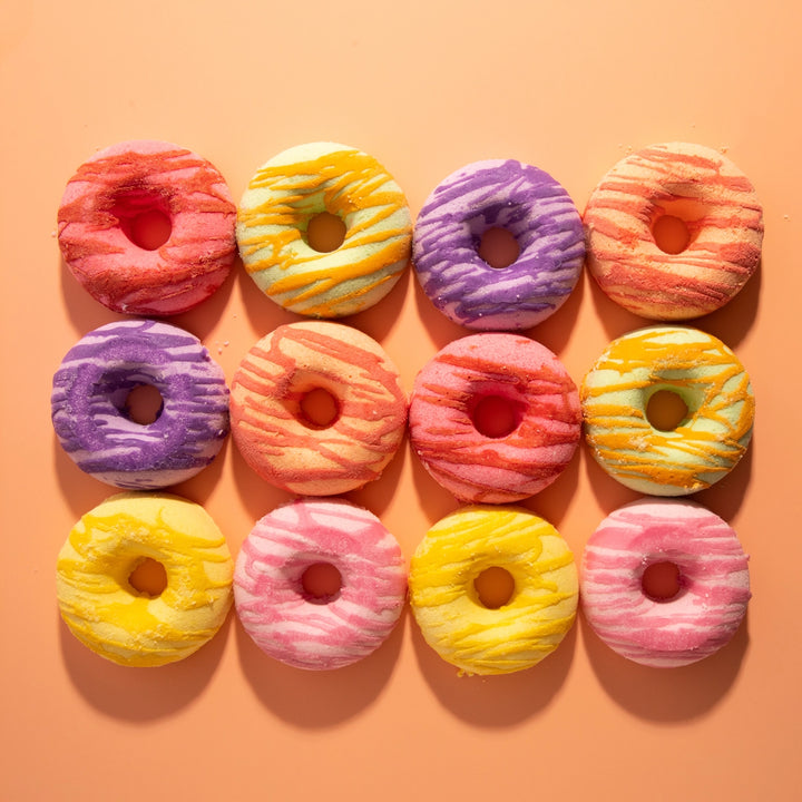 Colorful donut-shaped bath bombs arranged in a grid on an orange background
