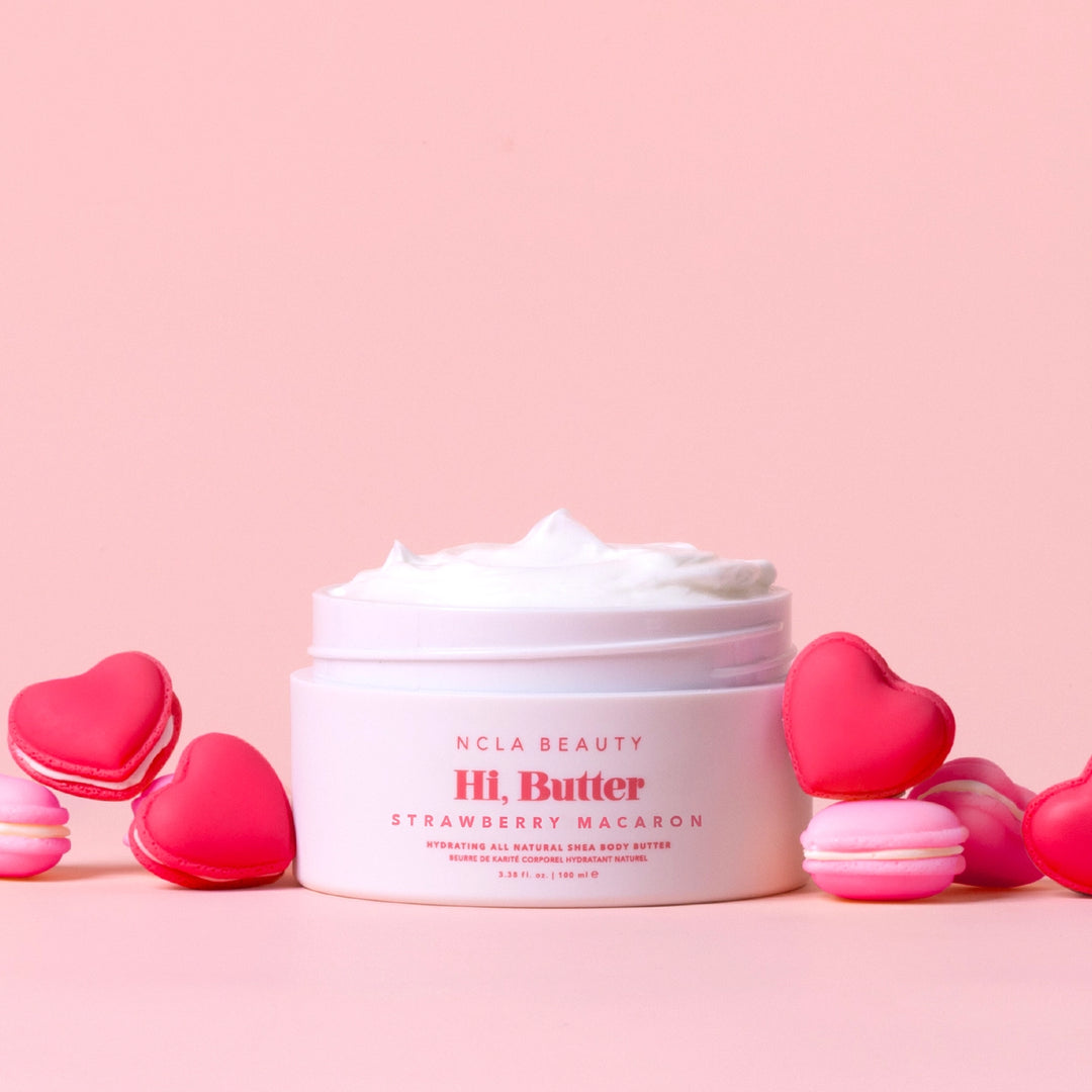 Jar of NCLA Beauty Hi. Butter Strawberry Macaron on a pink background with heart-shaped macarons.