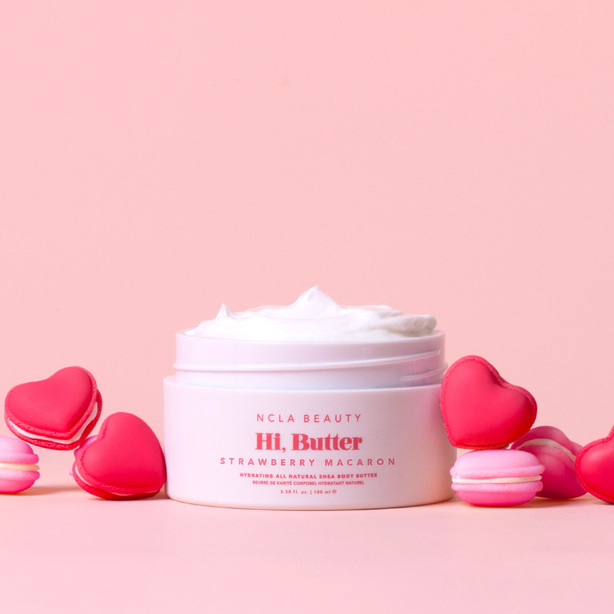 Jar of NCLA Beauty Hi. Butter Strawberry Macaron on a pink background with heart-shaped macarons.