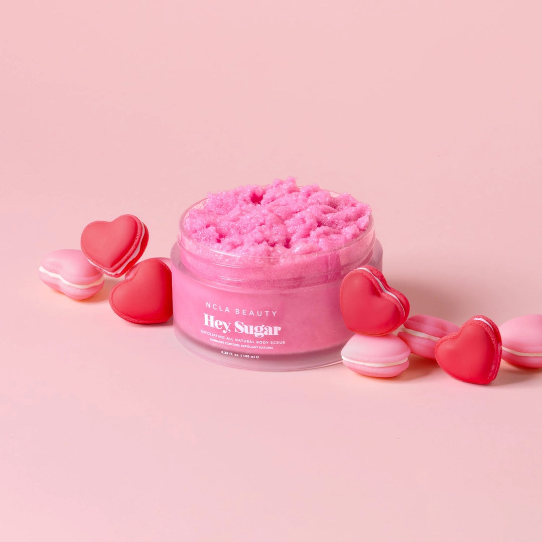 Pink sugar body scrub jar with heart-shaped containers on a pink background