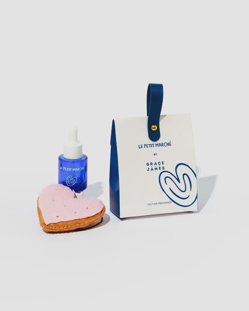 A box with a pink heart shortcake felt freshener with a blue bottle of fragrance
