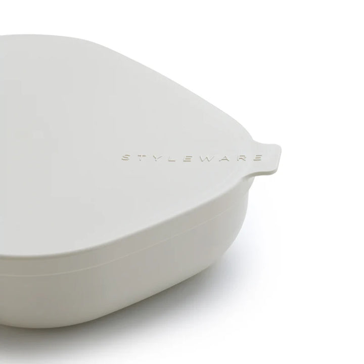 A close-up of a white silicone lid with a small tab on the right side, featuring the debossed brand name &