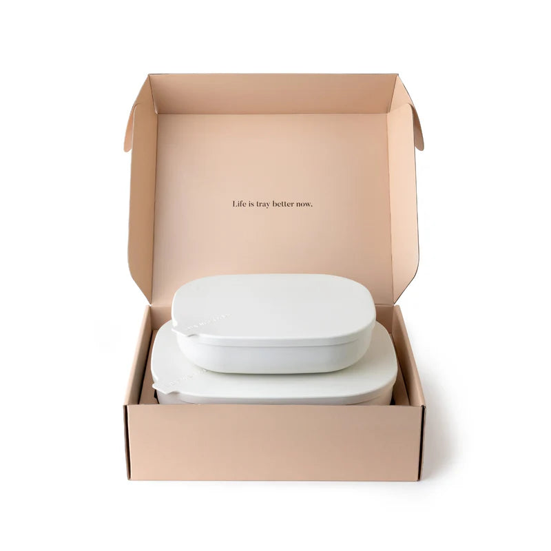 An open kraft paper box containing two stacked white oval containers, photographed on a clean white background. The inside lid has small printed text reading &