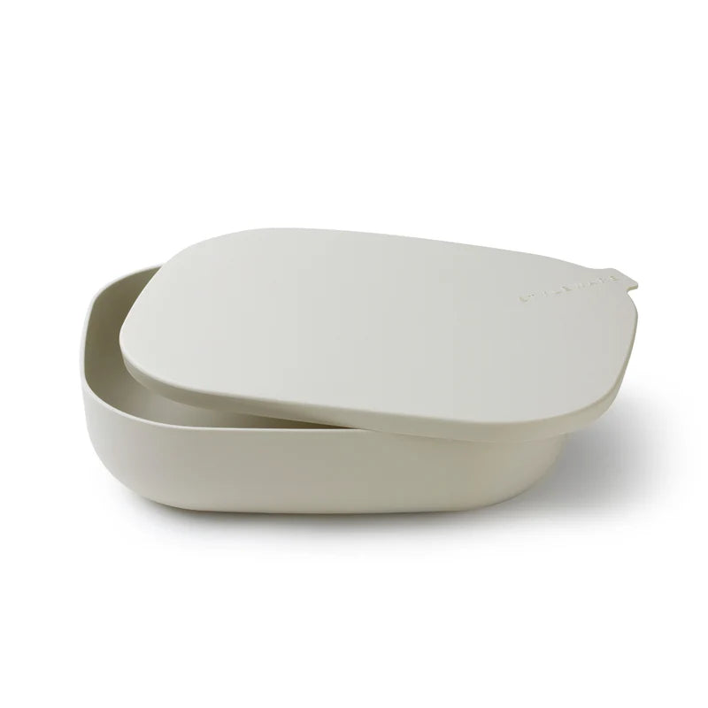 A minimalist beige silicone bento box with its matching lid resting on top, photographed on a clean white background.