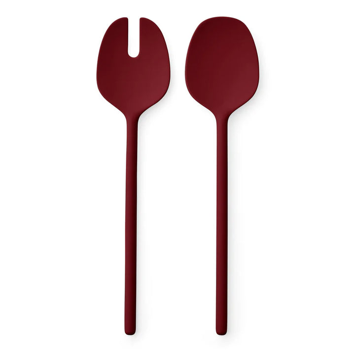 Two matte dark red serving utensils, one a salad server with a fork head and one a spoon, shown on a plain white background.