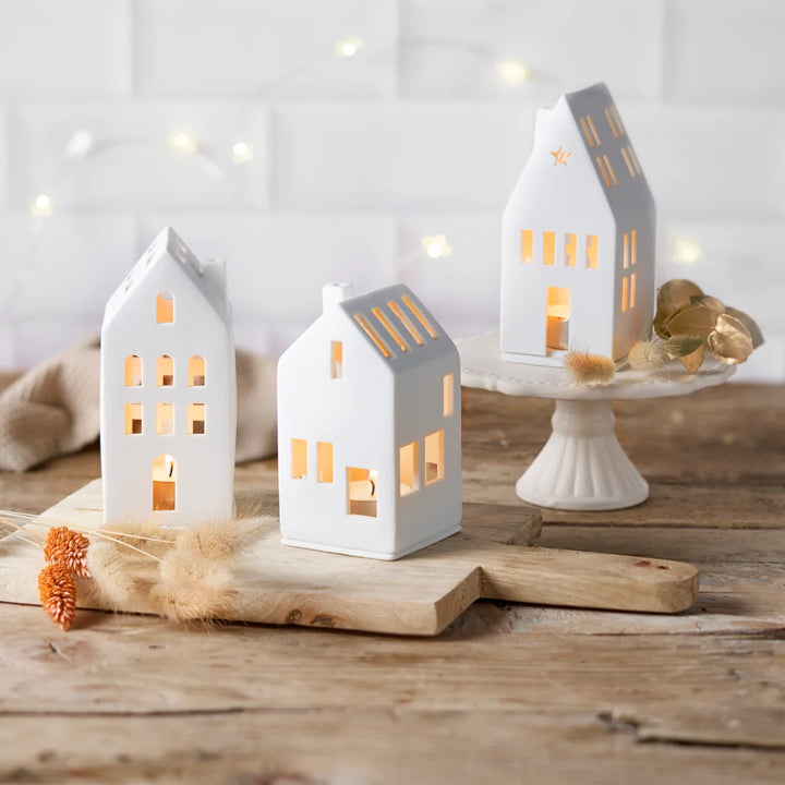 Three porcelain tealight houses on a wooden board with a white tiled wall background