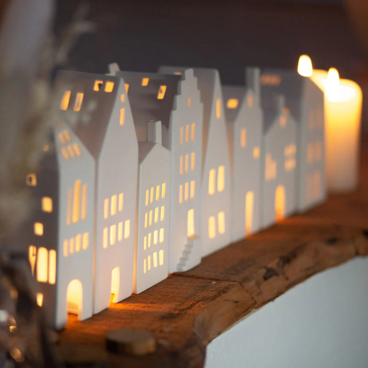 Collection of white tealight house candle holders on a wood shelf