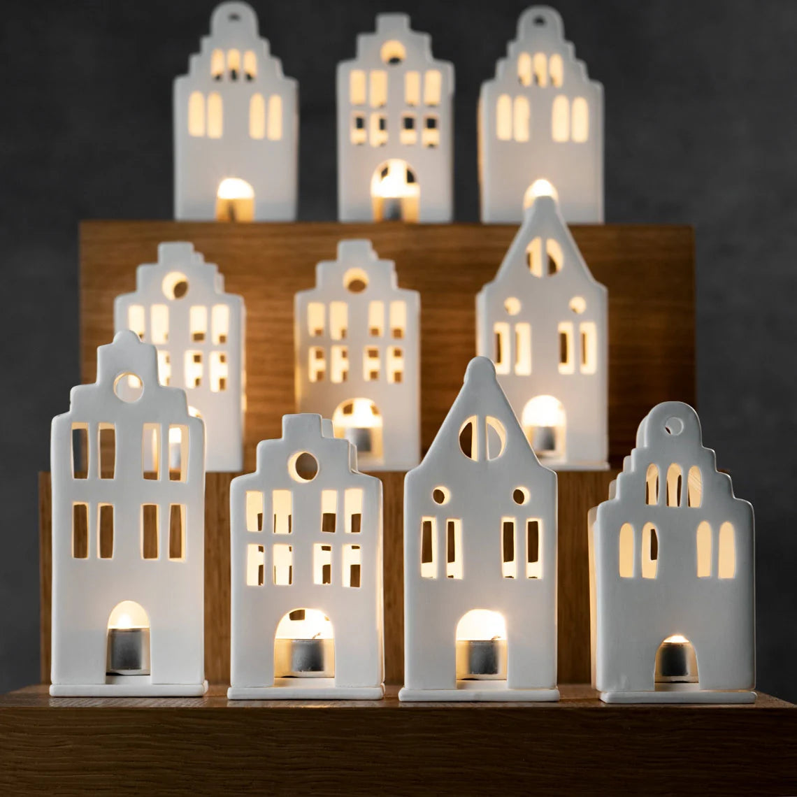 Collection of white porcelain tealight house candle holders arranged on timber shelves