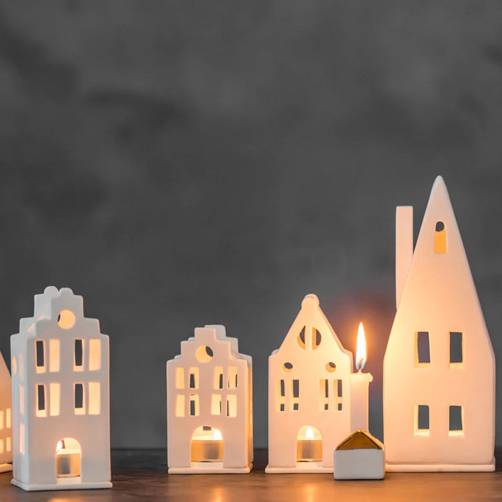 Set of four porcelain tealight house candle holders with lit candles on a grey background