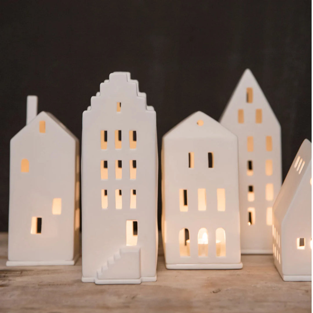 Collection of white tealight house candle holders on a timber surface with lit candles and a dark grey background