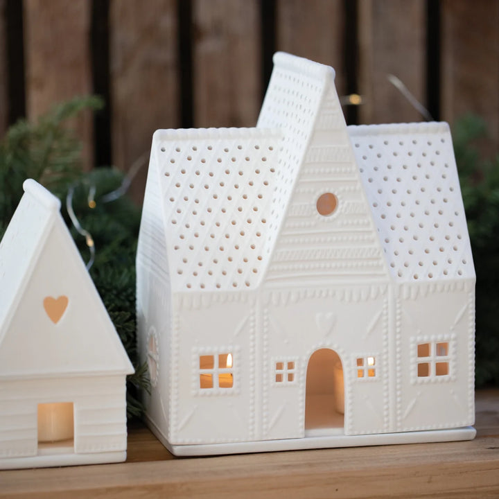 Two white ceramic house-shaped candle holders with small windows on a wooden surface.