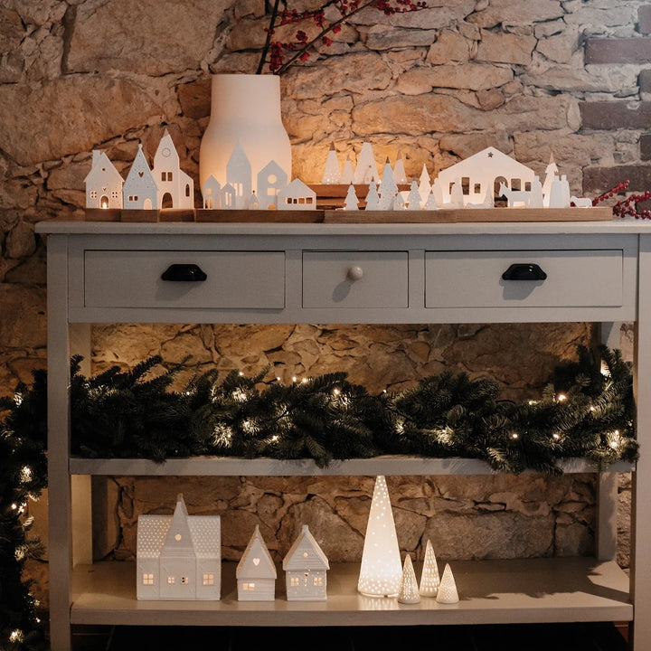 Collection of white porcelain tealight candle holders arranged on a side table with lit candles