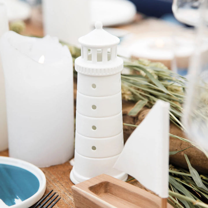 White porcelain tealight house candle holder lighthouse on a timber table with a lit candle