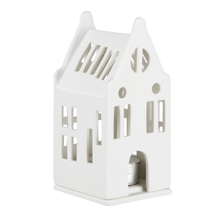 A white ceramic house-shaped candle holder with cutout windows and a small tealight candle visible inside, set against a plain white background.