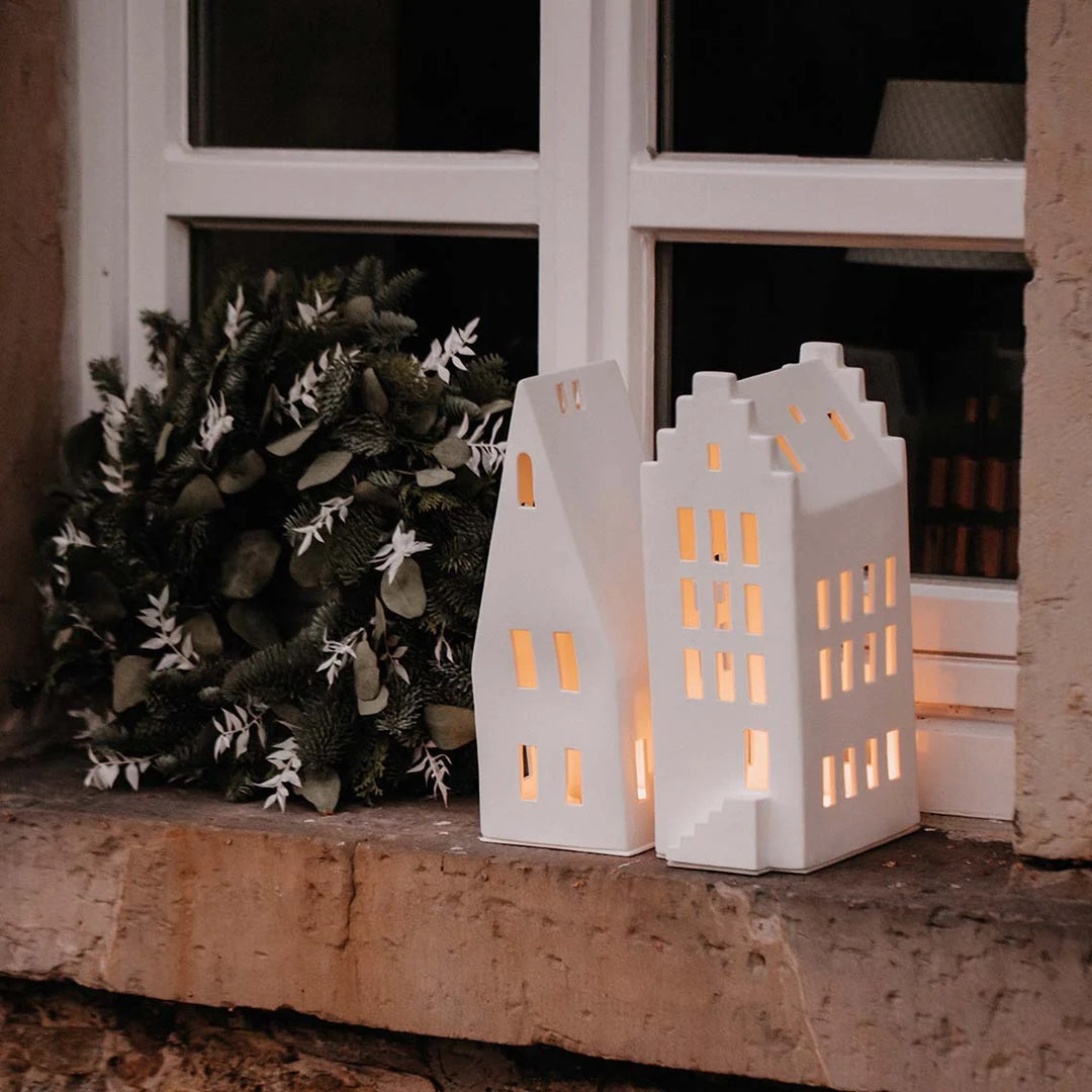 White porcelain tealight candle holders with lit candles on a windowsill with greenery
