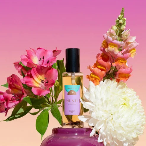 Room Spray with flowers on a gradient pink and orange background surrounded by fresh flowers